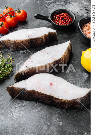 Raw halibut saltwater fish steak, with ingredients and rosemary herbs, on black dark stone table background Raw halibut saltwater fish steak, with ingredients and rosemary herbs, on black dark stone table background 85235721