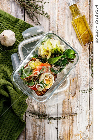 Delicious and healthy lunch with salmon fish fillet in a glass lunch box. Salad with smoked salmon, soft cheese, eggs, onion and vegetables. Seafood diet. Organic food Mediterranean lunch. Copy space 85239164
