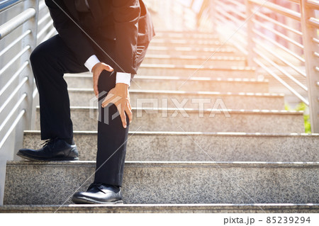 Businessman in a suit have the sore pain and painful knee problem expression and walk up and down on the stairway during go to office. Health care concept. Businessman in a suit have the sore pain and painful knee problem expression and walk up and down on the stairway during go to office. Health care concept. 85239294