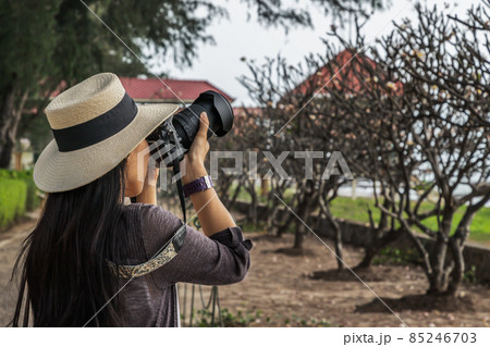 Young woman wearing a white hat and taking a camera to take pictures of the scenery on the sea beach. Young woman wearing a white hat and taking a camera to take pictures of the scenery on the sea beach. 85246703
