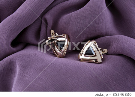 Golden earrings with the black stone on purple fabric background 85246830