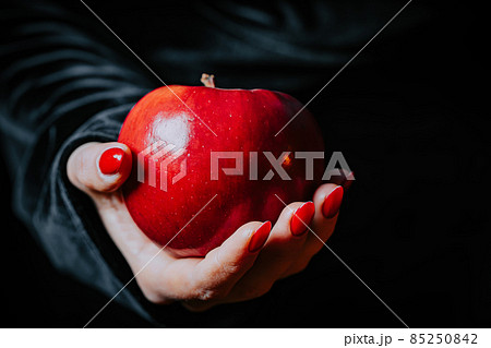 Witch woman in black offers red apple as symbol of temptation, poison. Fairy tale, white snow wizard 85250842