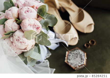 Wedding bouquet of white peonies, shoes and wedding rings on a wooden background 85264251