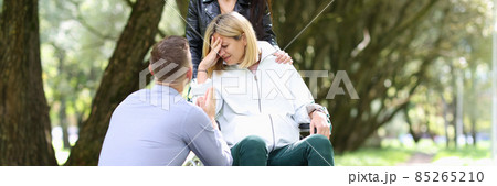 Disabled woman in wheelchair with her friend crying in front of man in park 85265210