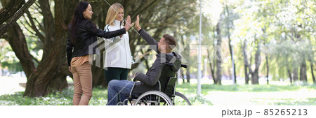 Disabled man in wheelchair giving five to female friends in park 85265213
