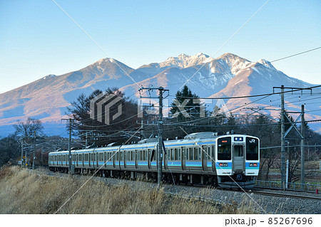 北杜市長坂町、八ヶ岳をバックに夕暮れの中央本線を行く列車・下り普通列車 85267696
