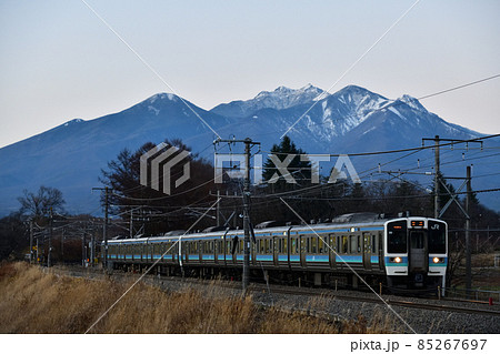 北杜市長坂町、八ヶ岳をバックに夕暮れの中央本線を行く列車・上り普通列車 85267697