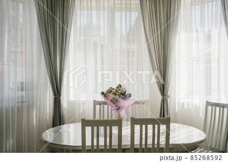 white oval table with a bouquet of flowers in a room with large windows. white oval table with a bouquet of flowers in a room with large windows. 85268592