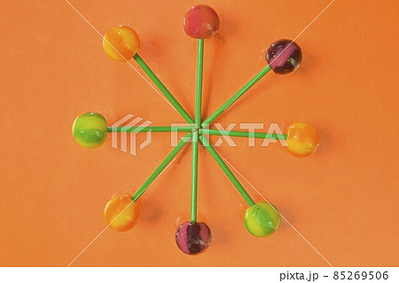 Colorful lollipops on green sticks in round. Multicolored candies on orange background, top view. Summer and pop art concept. Flat lay. Real reflection 85269506