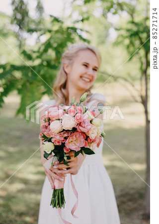 Bride with flowers outdoors. Portrait of a beautiful bride in a long white wedding dress with a bouquet of flowers in a forest park. Beautiful bride in fashion wedding dress on natural background.The Bride with flowers outdoors. Portrait of a beautiful bride in a long white wedding dress with a bouquet of flowers in a forest park. Beautiful bride in fashion wedding dress on natural background.The 85271714