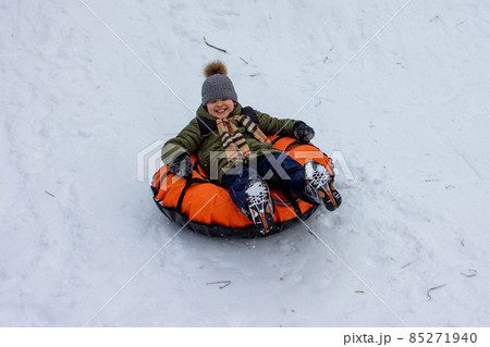 A child is tubing down the hill. Fun in the snow to ride down the hill on a tubing ice cheesecake. Earthly joyful fun, warm clothes. Boy is riding a tubing. Winter fun for children. High quality photo 85271940