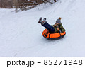 A child is tubing down the hill. Fun in the snow to ride down the hill on a tubing ice cheesecake. Earthly joyful fun, warm clothes. Boy is riding a tubing. Winter fun for children. High quality photo 85271948