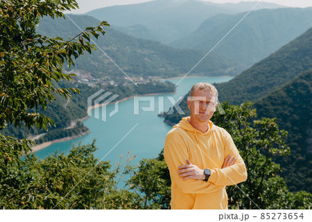 Man - Traveler on the background The famous Piva Canyon with its fantastic reservoir. View of road above Piva Lake (Pivsko Jezero) in Montenegro. man looks at river Piva, Montenegro. 85273654