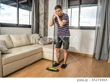 Sad and pensive man sweeping living room of his house. Sad and pensive man sweeping living room of his house. 85274464