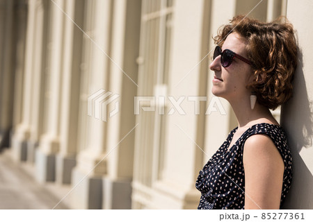 20 Year old white woman standing  against a classic wall in the sun 85277361