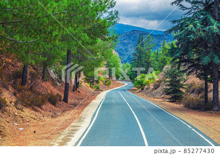 Asphalt serpentine road in Troodos mountain range with roadside fence and trees 85277430