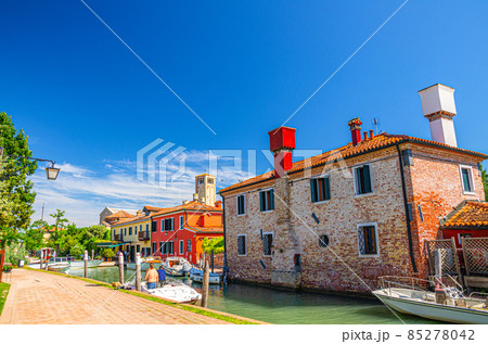 Torcello island with embankment promenade along water canal with motor boats and colorful buildings Torcello island with embankment promenade along water canal with motor boats and colorful buildings 85278042