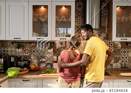 Happy young intercultural husband and wife standing by table and preparing food together Happy young intercultural husband and wife standing by table and preparing food together 85284638