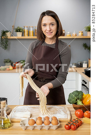 Happy young Caucasian woman in apron preparing spaghetti 85284713