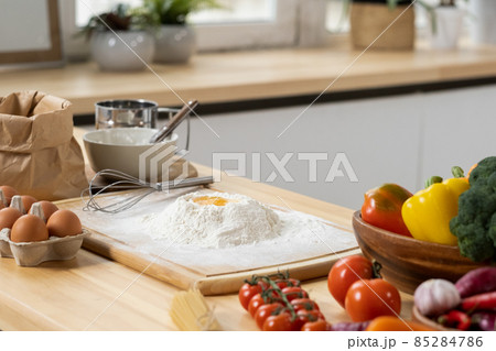 Pile of sifted flour with raw egg on top and other ingredients Pile of sifted flour with raw egg on top and other ingredients 85284786
