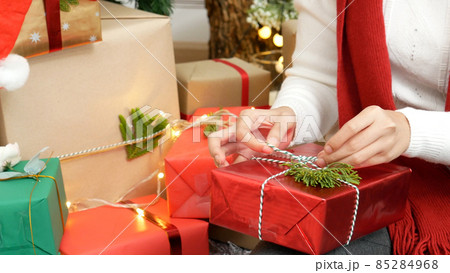 Close up woman hands wrap present gift in cozy living room. Woman wrapping christmas gift box under xmas tree. Asian woman decor bauble ball christmas tree in xmas holiday winter seasonal celebration 85284968