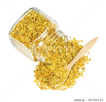 spoon in bee pollen spilled from overturned jar 85294115