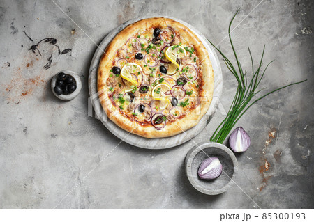 Tasty pizza with tuna, mozzarella, black olives and onion on marble round tray. Garnished on grey stone backdrop with pizza ingredients Tasty pizza with tuna, mozzarella, black olives and onion on marble round tray. Garnished on grey stone backdrop with pizza ingredients 85300193