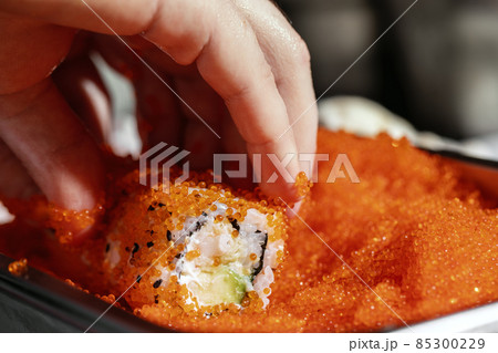 Closeup of chef hands rolling up sushi in flying fish roe (Tobiko) red caviar - focus on the roll. Closeup of chef hands rolling up sushi in flying fish roe (Tobiko) red caviar - focus on the roll. 85300229
