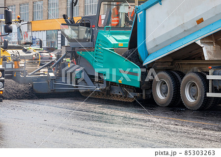 Construction of a new road, a truck pours hot asphalt into the bucket of an asphalt paver. Close-up. 85303263