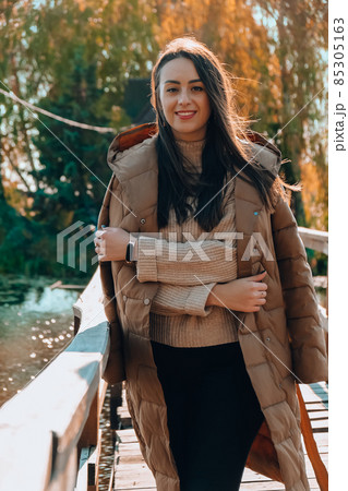 Beautiful brunette girl in autumn Park. Smiling young millennial woman in coat enjoying sunny weather in autumn fall weather. Outdoor portrait 85305163