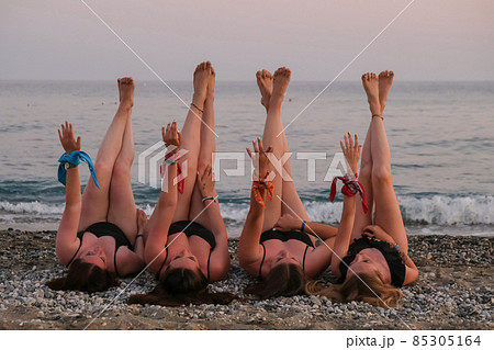 Four girls friends lying on beach stretching up slender legs sea island in the background having fun on vacation. Together. Woman on the beach relaxing concept. Beautiful vacation summer holiday 85305164