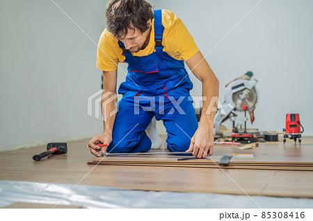 Man installing new wooden laminate flooring on a warm film floor. Infrared floor heating system under laminate floor 85308416