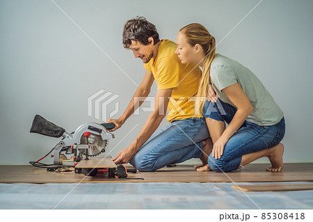 Married couple installing new wooden laminate flooring on a warm film floor. Infrared floor heating system under laminate floor 85308418