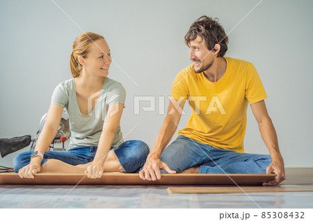 Married couple installing new wooden laminate flooring on a warm film floor. Infrared floor heating system under laminate floor 85308432