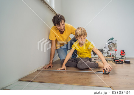 Father and son installing new wooden laminate flooring on a warm film floor. Infrared floor heating system under laminate floor Father and son installing new wooden laminate flooring on a warm film floor. Infrared floor heating system under laminate floor 85308434