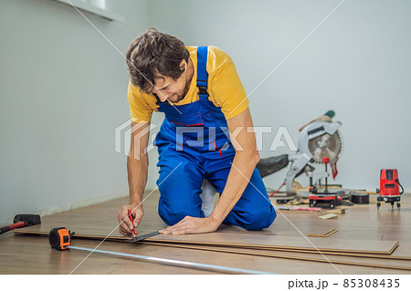 Man installing new wooden laminate flooring on a warm film floor. Infrared floor heating system under laminate floor 85308435