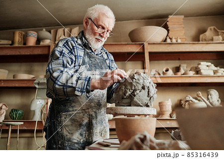 Senior male ceramist working with clay and making dishes by hands in pottery studio 85316439