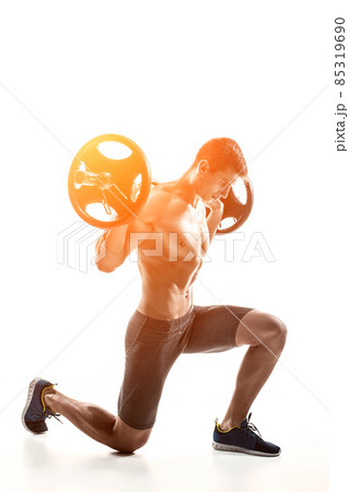 Muscular man standing on knee, holding barbell over his head Muscular man standing on knee, holding barbell over his head 85319690