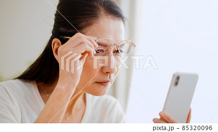老眼鏡でスマートフォンを覗くシニア女性 老眼鏡でスマートフォンを覗くシニア女性 85320096