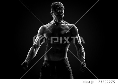 Sexy muscular man posing with naked torso on black background Sexy muscular man posing with naked torso on black background 85322275