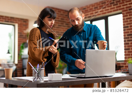 Colleagues looking at company strategy using laptop computer analyzing business paperwork Colleagues looking at company strategy using laptop computer analyzing business paperwork 85326472