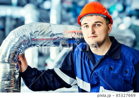 Portrait of young engineer in helmet in working environment at factory. Gas worker confidently looks 85327669