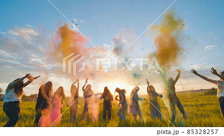 Cheerful girls toss up multi-colored powder at a beautiful sunset. 85328257
