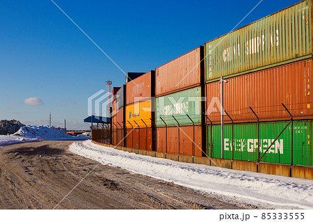 Klaipeda, Lithuania - 02 06 21: colored cargo export container in the warehouse of Klaipeda port docks, yellow crane and snowy winter road, deep blue shadows. Sunny colorful photo 85333555
