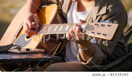 Man playing guitar at sunset lake, Close-up male hand playing on acoustic guitar outdoor with sunlight reflected on the water surface. 85339165