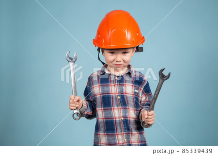 A cute funny little boy in an orange hard hat posing funny, holding wrenches A cute funny little boy in an orange hard hat posing funny, holding wrenches 85339439