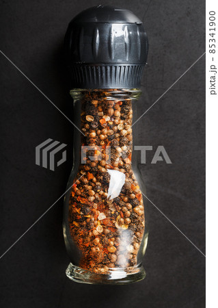 A mixture of seasonings, spices and herbs in a glass mill on a black background. 85341900