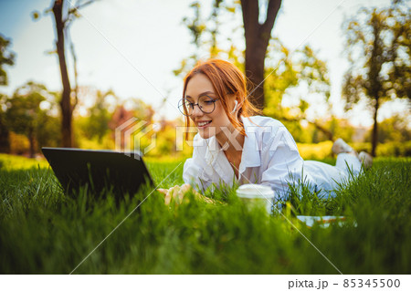 beautiful smiling girl student uses laptop pc while lying on the grass outdoors. Education concept beautiful smiling girl student uses laptop pc while lying on the grass outdoors. Education concept 85345500