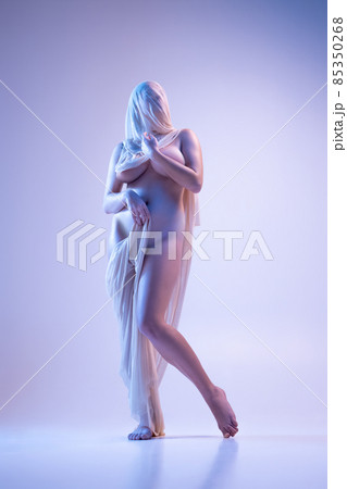 Full-length portrait of young woman in transparent veil posing naked isolated over purple background in neon lights 85350268