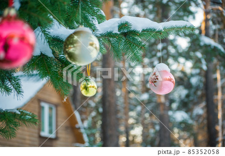 Spruce tree with Christmas toys in front of a wooden house Spruce tree with Christmas toys in front of a wooden house 85352058